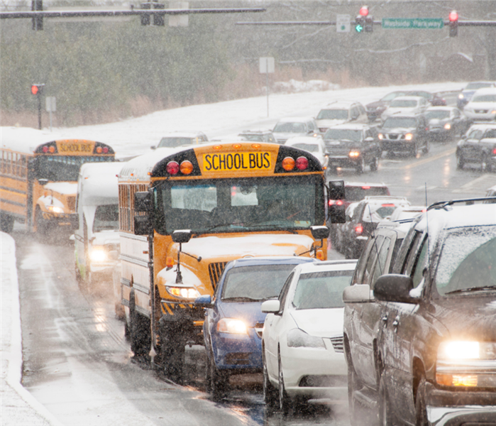 A line of cars in traffic during a winter storm with snow covering each one and the road